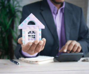 Man shown with calculator holding toy house to illustrate down payment and mortgage assistance